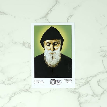 Portrait of Saint Charbel, a religious figure with a beard and black headscarf on a marble background